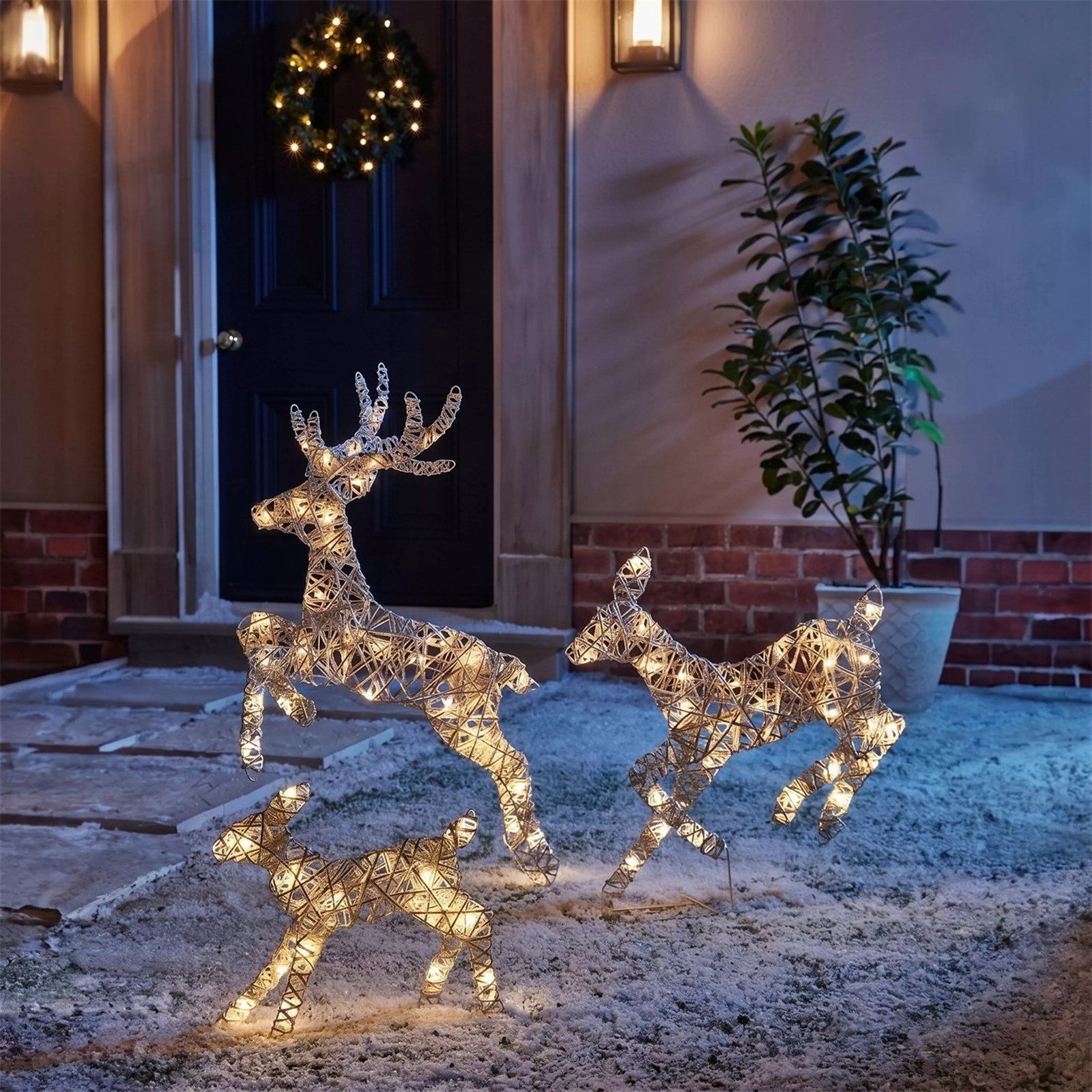 Three light-up reindeer glowing outside a front door